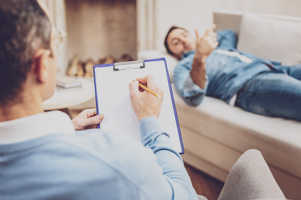 therapist taking notes while man talks on couch in men's rehab program